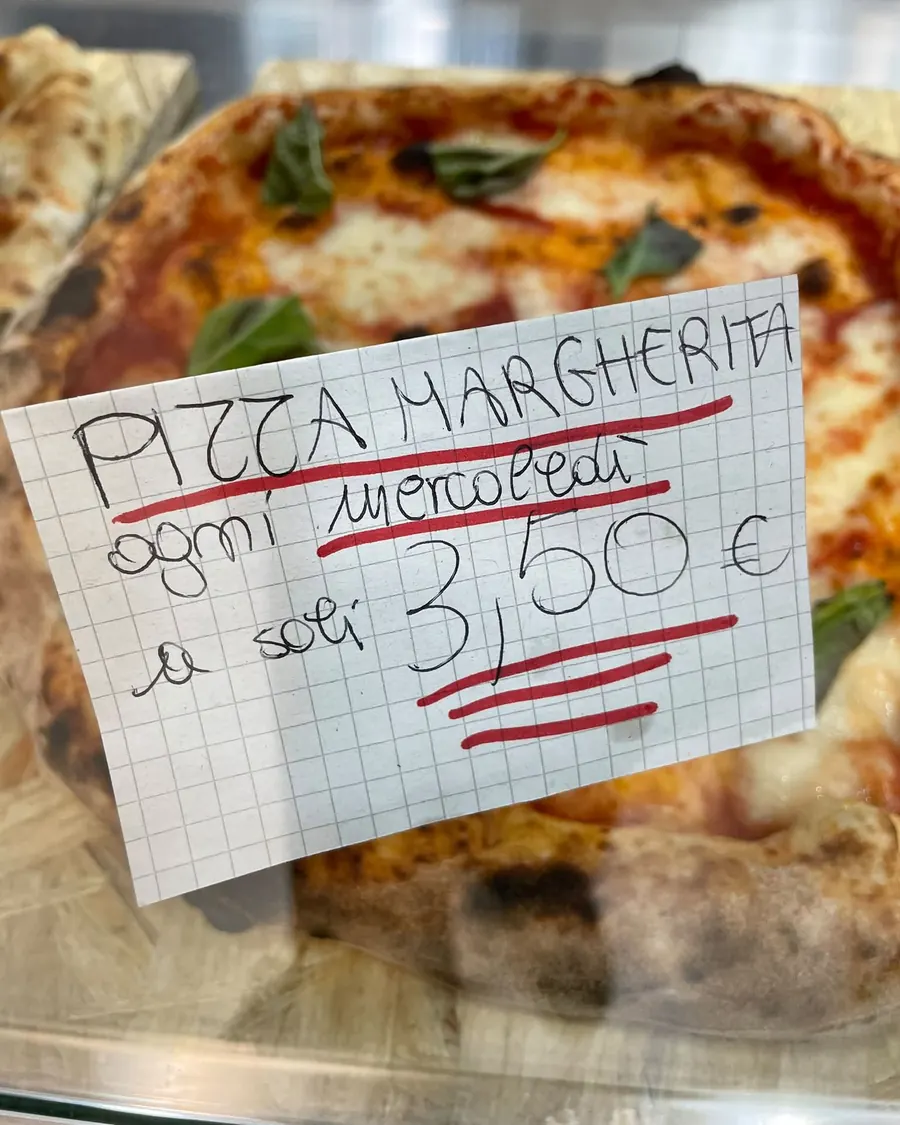 Una margherita nella vetrina del locale, con il cartello scritto a mano: pizza margherita ogni mercoledì a soli 3,50 euro